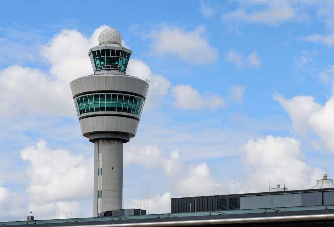 An airport control tower with a glazed cab and a radome on top, under a blue sky with clouds.